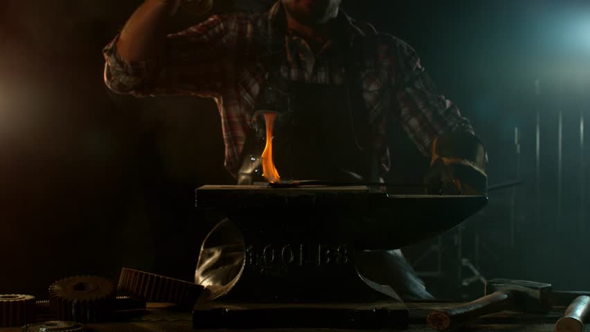 Close-up of blacksmith forging glowing hot iron on anvil with flying sparks. Super slow motion filmed on high-speed cinema camera at 1000 fps