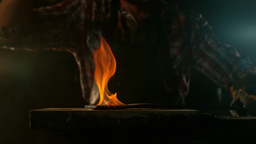 Close-up of blacksmith forging glowing hot iron on anvil with flying sparks. Super slow motion filmed on high-speed cinema camera at 1000 fps