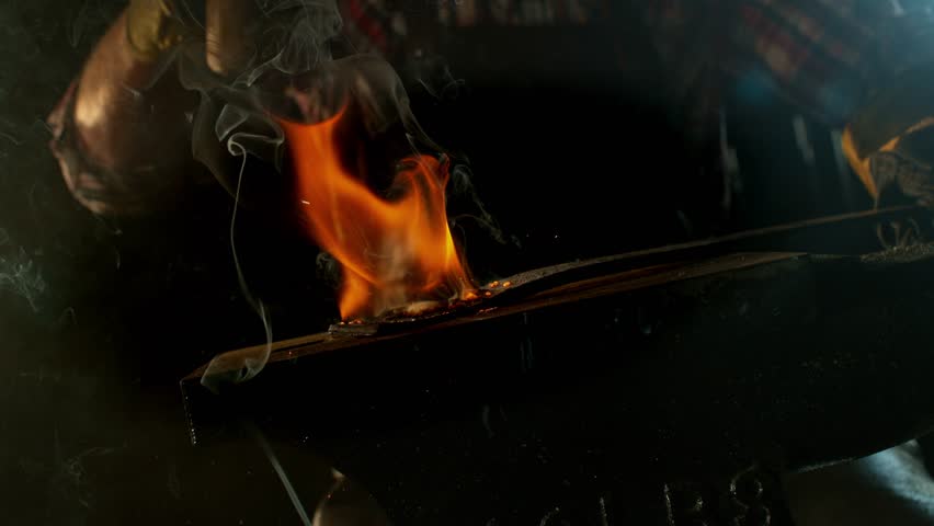 Close-up of blacksmith forging glowing hot iron on anvil with flying sparks. Super slow motion filmed on high-speed cinema camera at 1000 fps