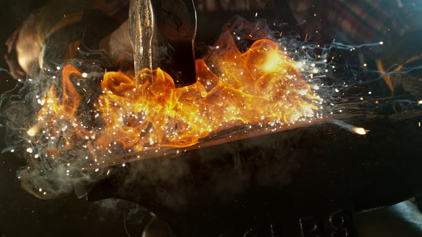 Close-up of blacksmith forging glowing hot iron on anvil with flying sparks. Super slow motion filmed on high-speed cinema camera at 1000 fps