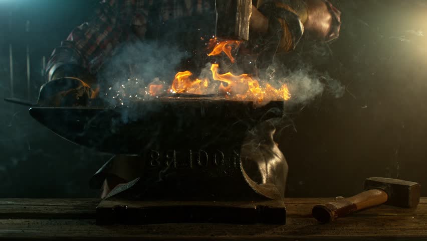 Close-up of blacksmith forging glowing hot iron on anvil with flying sparks. Super slow motion filmed on high-speed cinema camera at 1000 fps