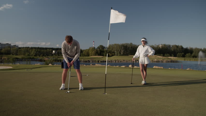 Male golfer puts ball in hole as woman companion watching - Powered by Shutterstock - Get 15% off with code: PIKWIZARD15