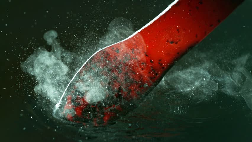 Close-up of glowing hot iron being quenched in cold water. Steam rises, water bubbles and sizzles. Captured in super slow motion with high-speed camera. Concept of metal forging and cooling.