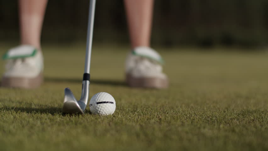 Lady golfer hits golf ball with steel driver on putting green