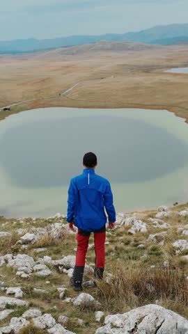 Hiker with arms raised looking at mountain lake in Durmitor National Park, Montenegro, during autumn. Outdoor adventure and freedom concept. High quality 4k footage