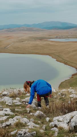 A man with German and Australian Shepherd sitting on a rocky hill overlooking a turquoise mountain lake in Durmitor National Park, Montenegro, autumn. High quality 4k vertical footage