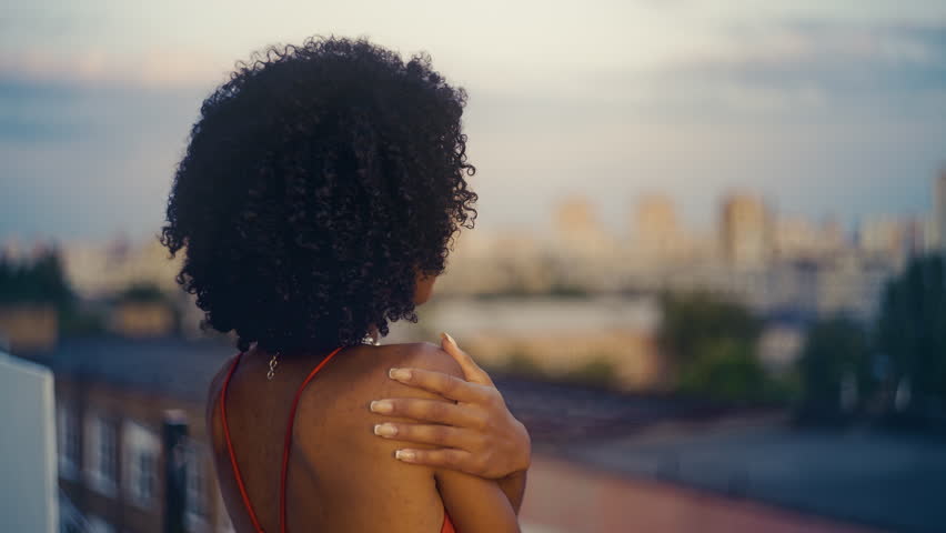 Depressed Black woman in elegant dress watching sunset from rooftop, solitude