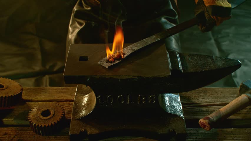 Cinematic close-up of blacksmith forging glowing hot iron on anvil with sparks flying. Shot in dramatic lighting on dark background with high-speed camera at 1000fps. Camera in motion. Speed Ramp.