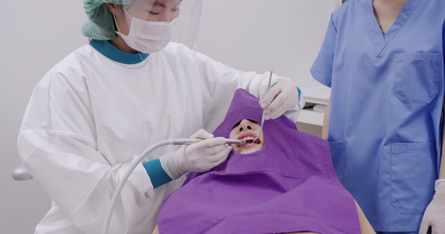Slowmotion footage of dental composite filling being applied under curing light as asian female patient lies in chair while dentist and assistant perform procedure in clinical room