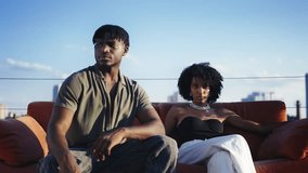 Black couple in stylish outfits sitting on red couch on rooftop, fashion video - Powered by Shutterstock - Get 15% off with code: PIKWIZARD15