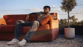 Black man in stylish clothing sitting on red couch on rooftop, model photoshoot - Powered by Shutterstock - Get 15% off with code: PIKWIZARD15