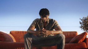 Young African American man sitting on red couch on rooftop, modeling video shoot - Powered by Shutterstock - Get 15% off with code: PIKWIZARD15