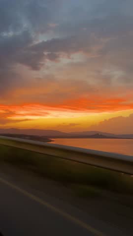 A scenic drive along a coastal highway in Georgia with a glowing orange and yellow sunset reflecting over calm waters.