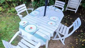 The woman sets the outdoor table with nice plates and cutlery. The table has a white tablecloth with green thin stripes. The woman is wearing black clothes and has long hair. - Powered by Shutterstock - Get 15% off with code: PIKWIZARD15