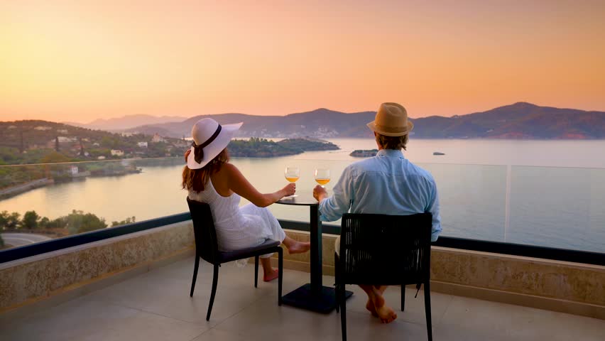 A elegant holiday couple enjoys the beautiful summer sunset in the mediterranean sea with a glass of wine, romantic honeymoon vacation concept