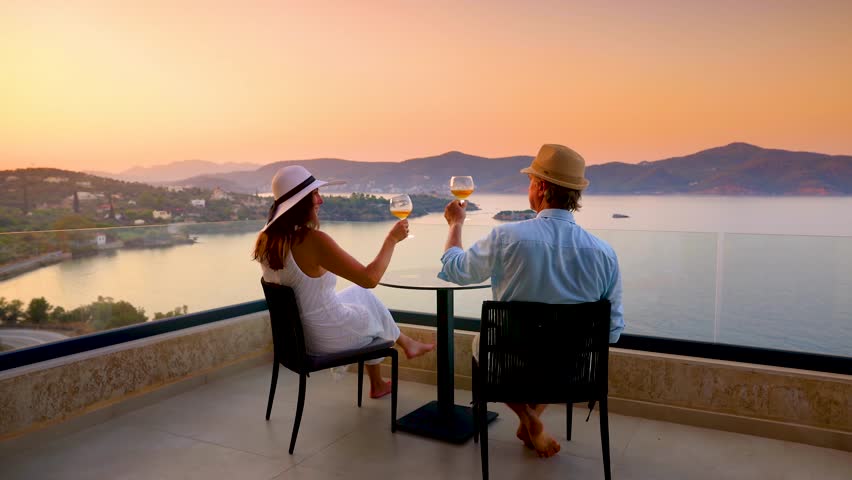 A elegant holiday couple enjoys the beautiful summer sunset in the mediterranean sea with a glass of wine, romantic honeymoon vacation concept