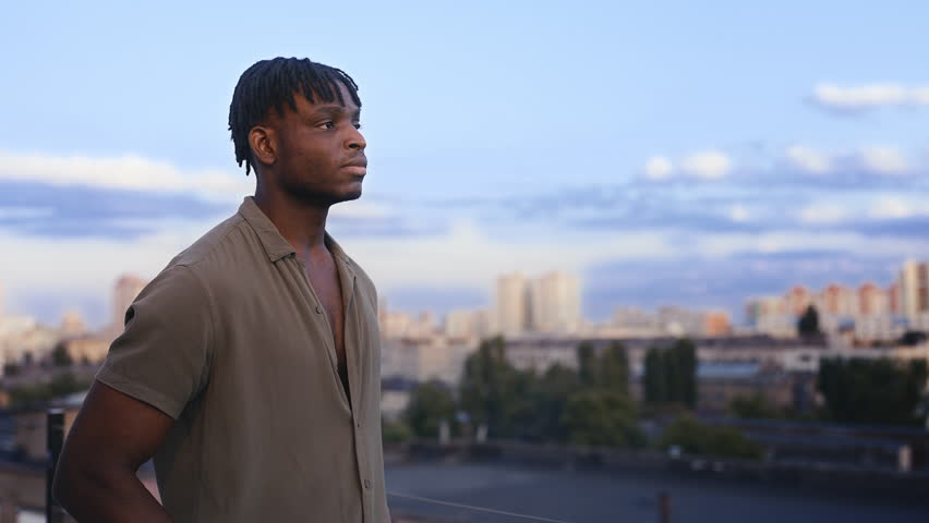 Unhappy African American man thinking about debts, looking at city from rooftop