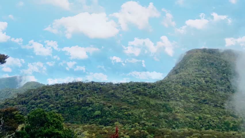A green and beautiful mountain landscape in West Java, Indonesia. The mountain atmosphere is cool and peaceful, with white clouds floating across the blue sky.