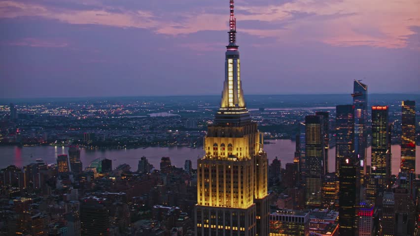 Aerial view of the Empire State Building in Manhattan, New York City during evening skyline. Iconic landmark surrounded by skyscrapers, lights, and cityscape. Perfect for travel, architecture