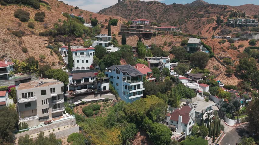 Aerial wide reverse pullback shot of hillside homes in the upscale neighborhood of Hollywood Hills in Los Angeles, California. 4K