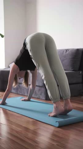Downward facing dog pose on mat in living room, woman doing morning yoga, stretching for wellness