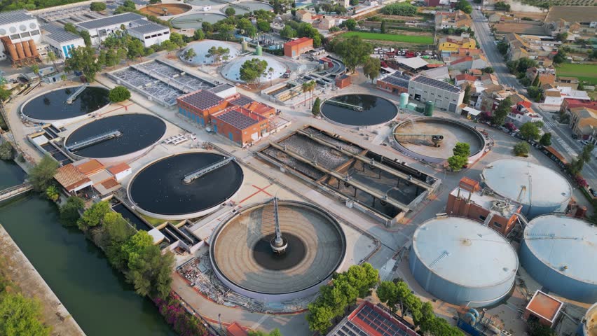 Wide aerial drone view of wastewater treatment plant with canal and road nearby