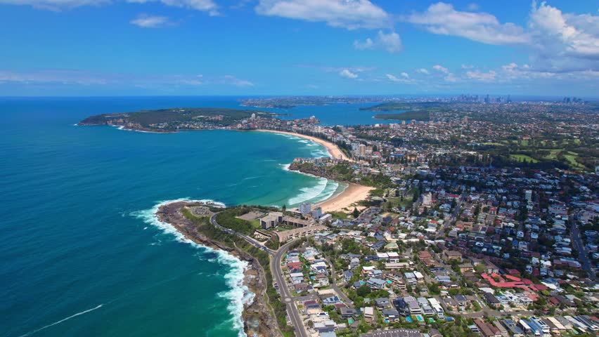 A spectacular aerial view of Sydney s coastline, featuring a stunning crescent-shaped beach with golden sands and turquoise waters. The image captures the lush greenery, residential areas