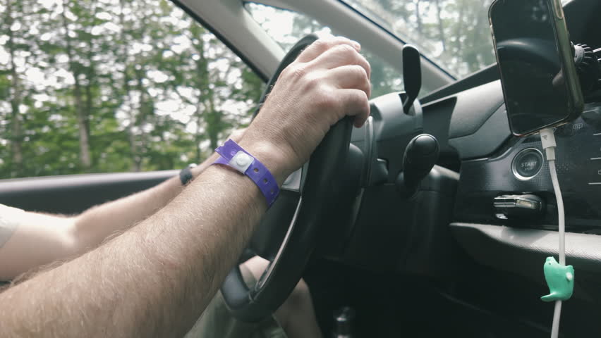 Close-up shot of a man's hands turning a steering wheel while driving.
