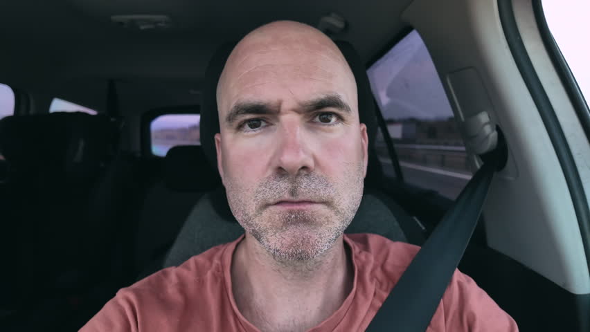 Close-up of a man's face while driving, serious facial expression.
