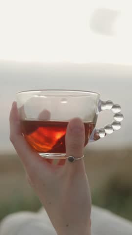 In a serene moment, I am gently holding a glowing cup of fragrant tea against a stunning seaside backdrop