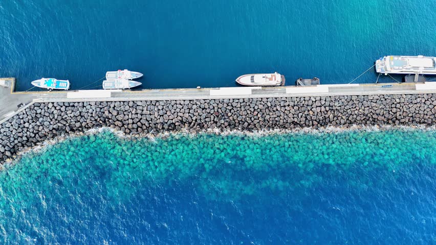 Stunning aerial view of a serene dock with boats resting against a vibrant turquoise sea at midday in a tranquil coastal setting