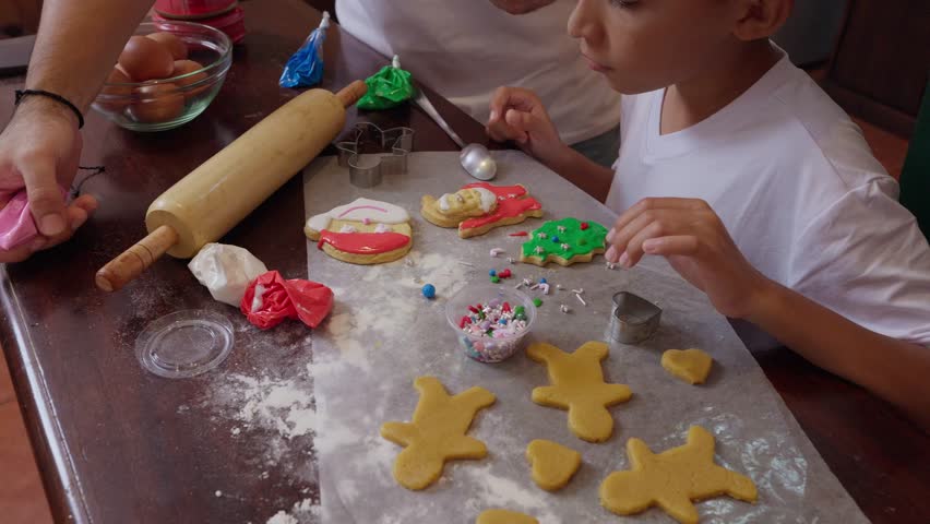 Child and adult decorating Christmas cookies with icing and sprinkles