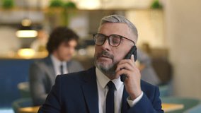 Senior grey-haired businessman in formal suit and glasses making phone call while sitting in restaurant - Powered by Shutterstock - Get 15% off with code: PIKWIZARD15