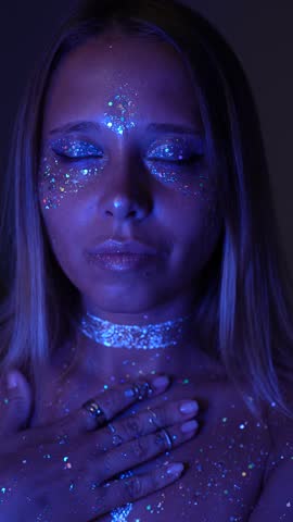 A young starseed cosmic woman alien places her hand on her heart, bathing in blue and violet glow. Her gaze awakens remembrance, she embodies a divine extraterrestrial essence, returning to herself