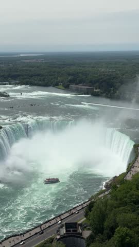 PAN SLOW MOTION SHOT - A tour boat loaded with tourists in red ponchos cruises towards to mist at the base of the Horseshoe Falls in Niagara Falls, Ontario, Canada.