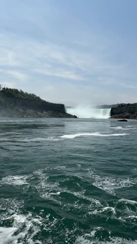 PAN SHOT - A tour boat loaded with tourists in blue ponchos at the base of the American Falls and Bridal Veil Falls in Niagara Falls, Ontario, Canada.