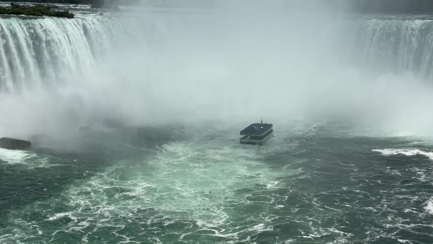 SLOW MOTION SHOT - A tour boat loaded with tourists in blue ponchos cruises towards the mist at the base of the Horseshoe Falls in Niagara Falls, Ontario, Canada.