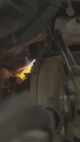 A close-up shot of a mechanical or industrial part being subjected to bright light and heat, possibly during a welding or cutting process. The scene shows flashes and dust, creating a dynamic and acti