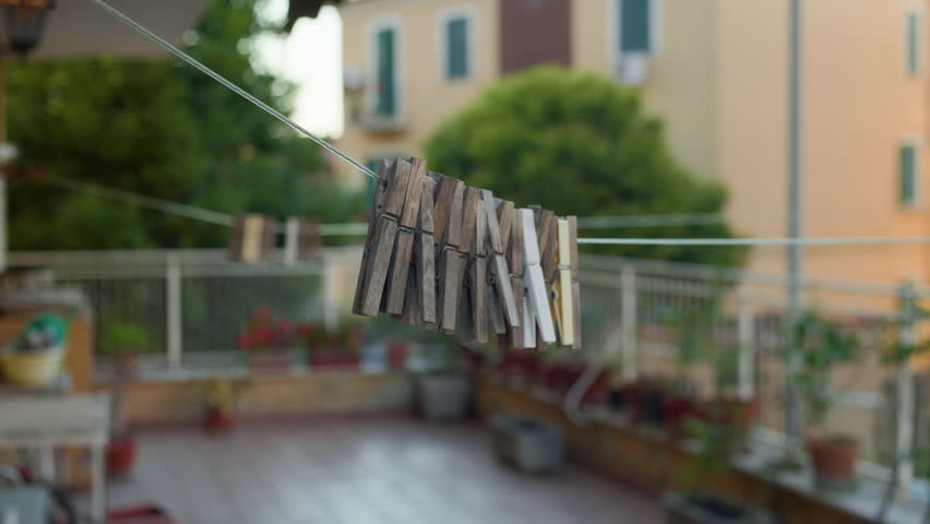 Handheld left-to-right close-up of clothespins on a clothesline in sharp focus, with a blurred city balcony in the background.