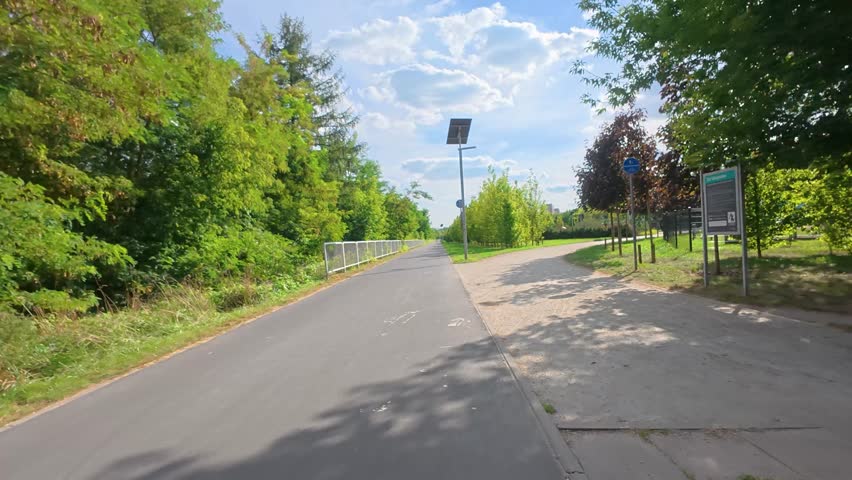 Point of view shot of riding a bicycle along a path surrounded by green trees in summer.