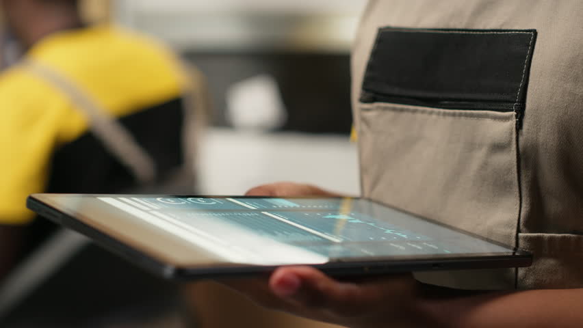 Close up of distribution hub worker overseeing supply chain process for e-commerce. Reviewing logistics and shipping data on tablet, updating tracking labels for order fulfillment. Camera B.