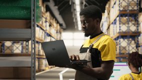 Black male staff verifying inventory pallets in e-commerce logistics center. Accurate order processing on laptop and packaging for quick shipping in large scale warehouse setting. Camera B. - Powered by Shutterstock - Get 15% off with code: PIKWIZARD15