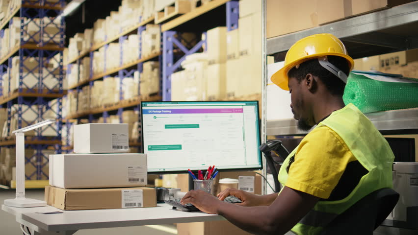 Black depot clerk reviewing inventory data on tracking software for distribution system, busy logistics hub stock room with organized racks. Online retail fulfillment and supply chain. Camera A.