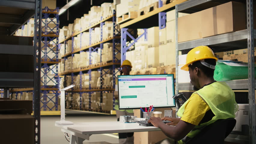 Young man using scanner on barcodes and applying tags in distribution hub. Organized shelving, package labels and route planning support efficient shipment and order fulfillment. Camera A.
