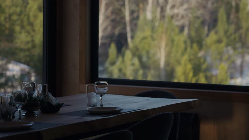 Set up for dinner with elegant utensils on the table opposite the window. Interior design of modern dining room.