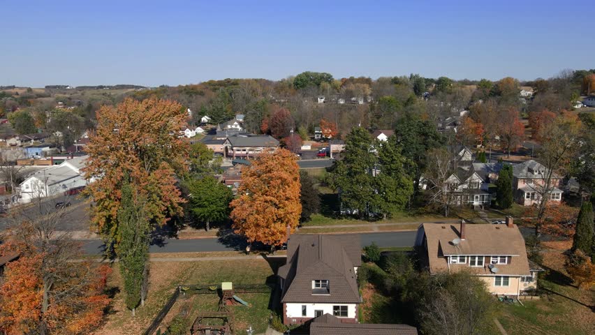 Drone view of a quiet Midwestern town in Minnesota during fall. Tree-lined streets, residential houses, and small public buildings framed by autumn foliage under a clear sky.