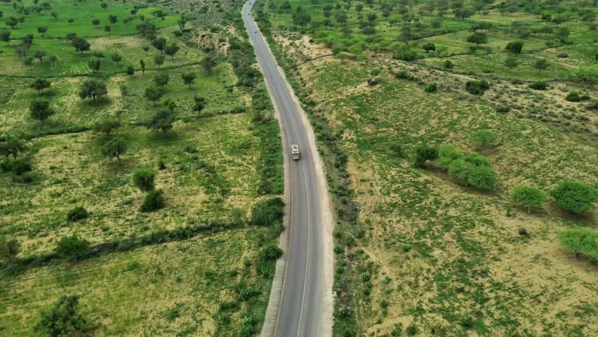 
Aerial view of winding road through green semi-arid landscape with scattered trees and fields.