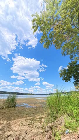 A scenic timelapse video of white clouds drifting across a blue summer sky above Pohick Bay in Virginia, with trees and shoreline vegetation framing the natural landscape.
