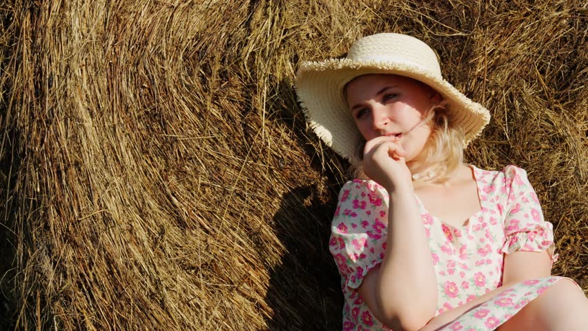 Portrait of a happy young woman in a hat on the background of a haystack. The concept of agriculture, simple village life.	