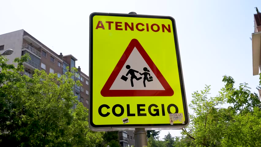 A Spanish traffic sign warns drivers to be cautious. The yellow sign reads "Atención Colegio" (Attention, School) and indicates a school zone where children may be present.